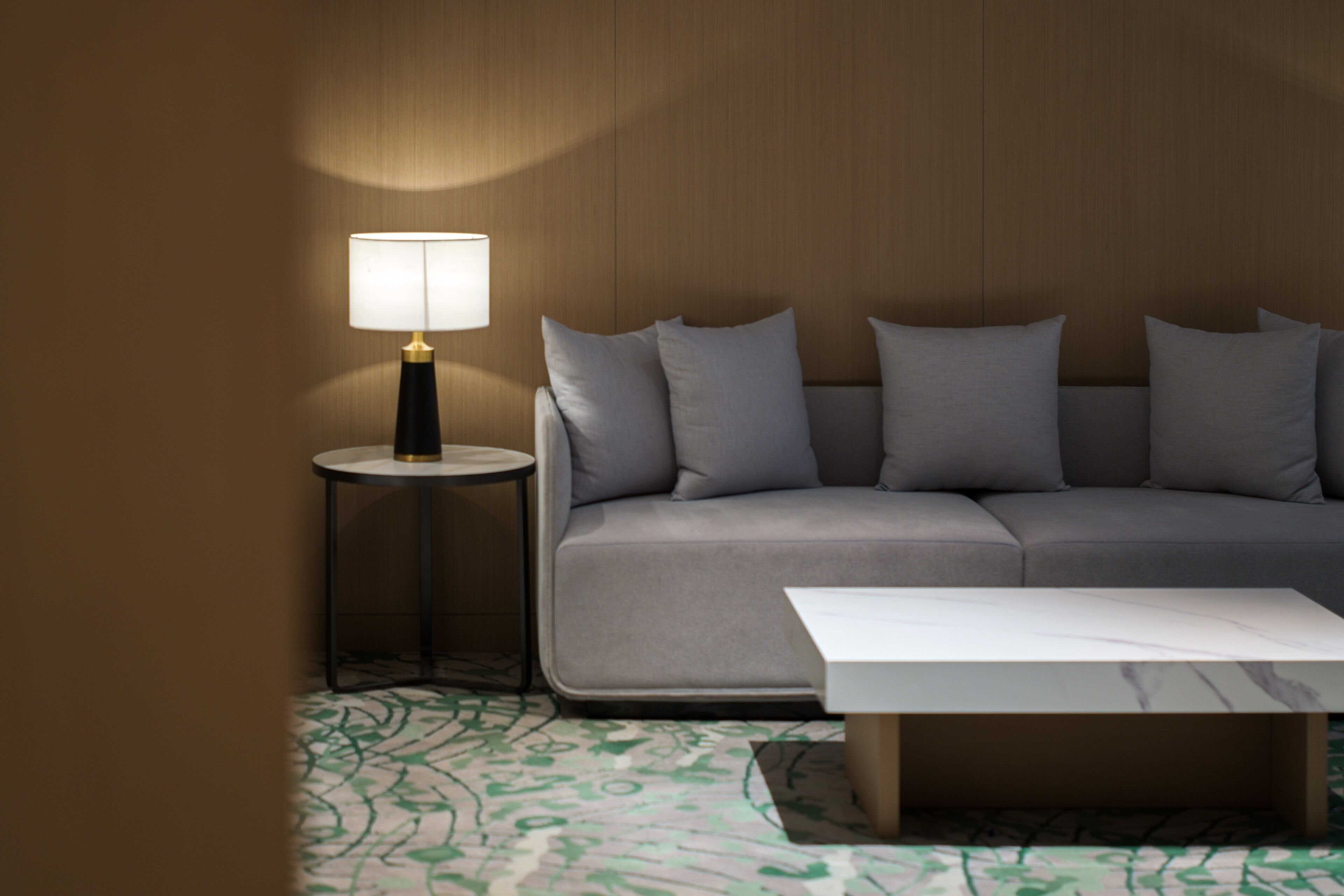 Een moderne woonkamer met een grijze bank, een ronde bijzettafel met een lamp en een witte salontafel.