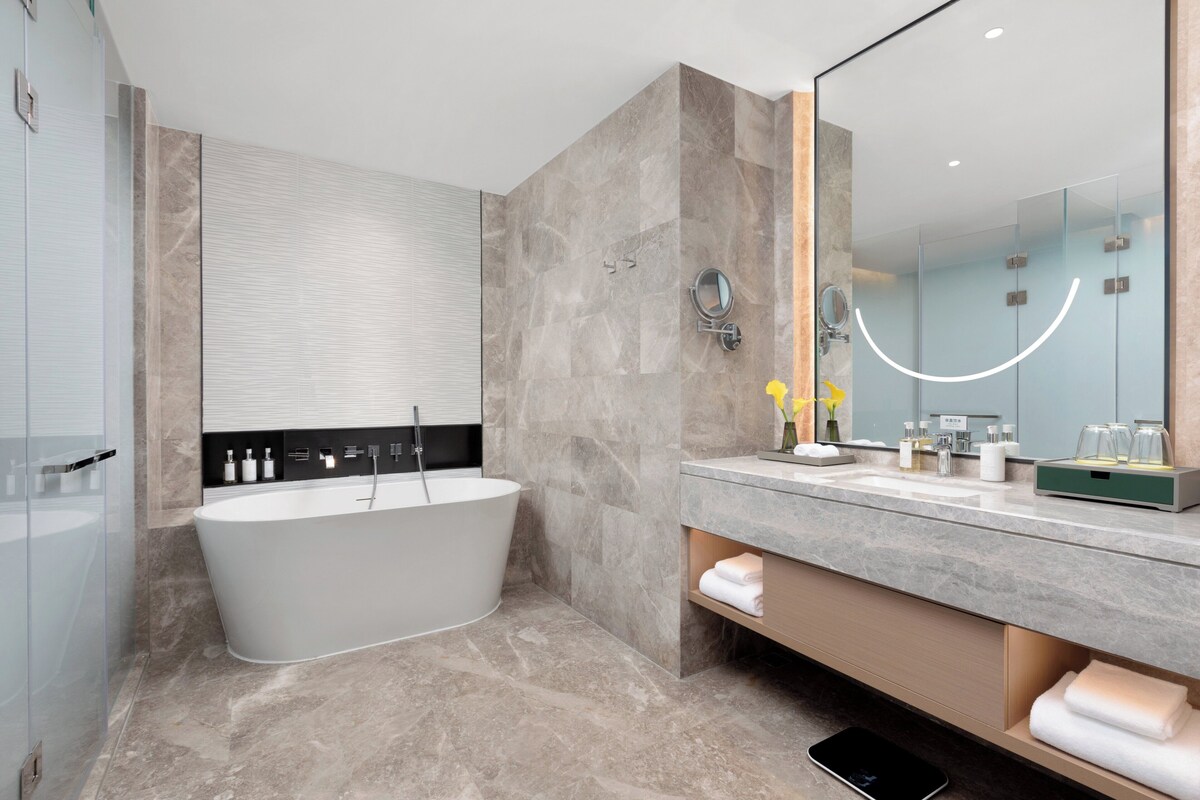 Un baño moderno con una bañera independiente, un espejo grande y un tocador con lavabo y espacio para toallas.
