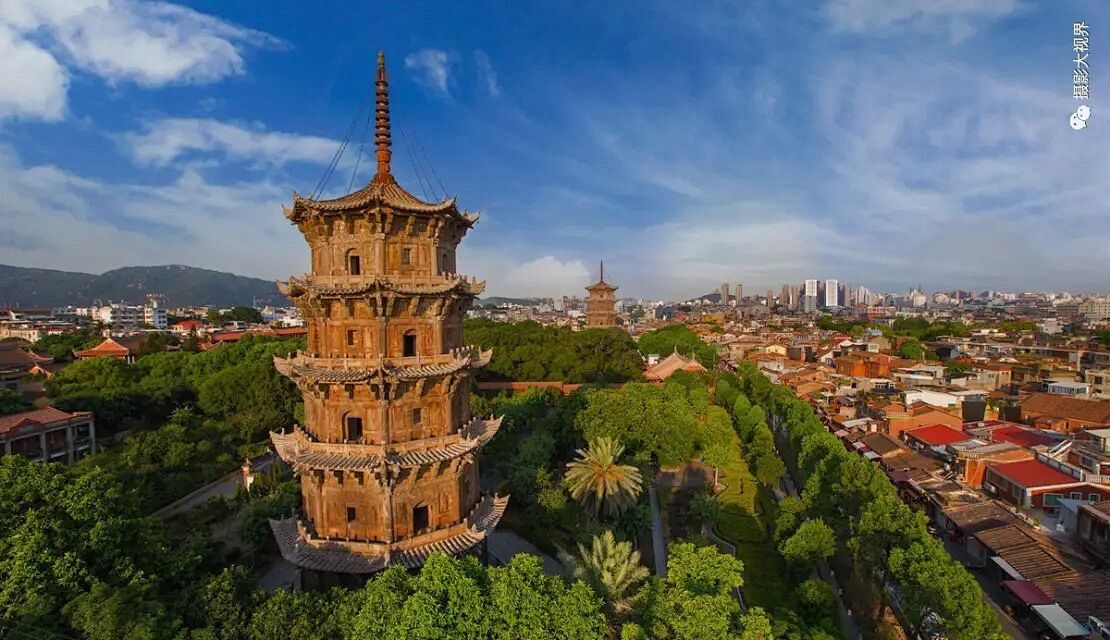 A traditional multi-tiered pagoda surrounded by lush greenery and a cityscape in the background.