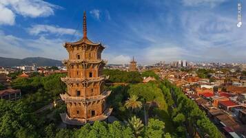 Um pagode tradicional de vários níveis, rodeado por vegetação exuberante e uma paisagem urbana ao fundo.
