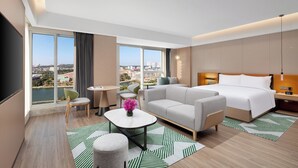 Een moderne hotelkamer met een groot raam, een bank, een bed, een klein tafeltje en een stoel.