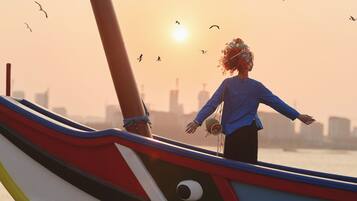 Una persona de pie en un bote, con los brazos extendidos, mirando al atardecer con aves volando al fondo.