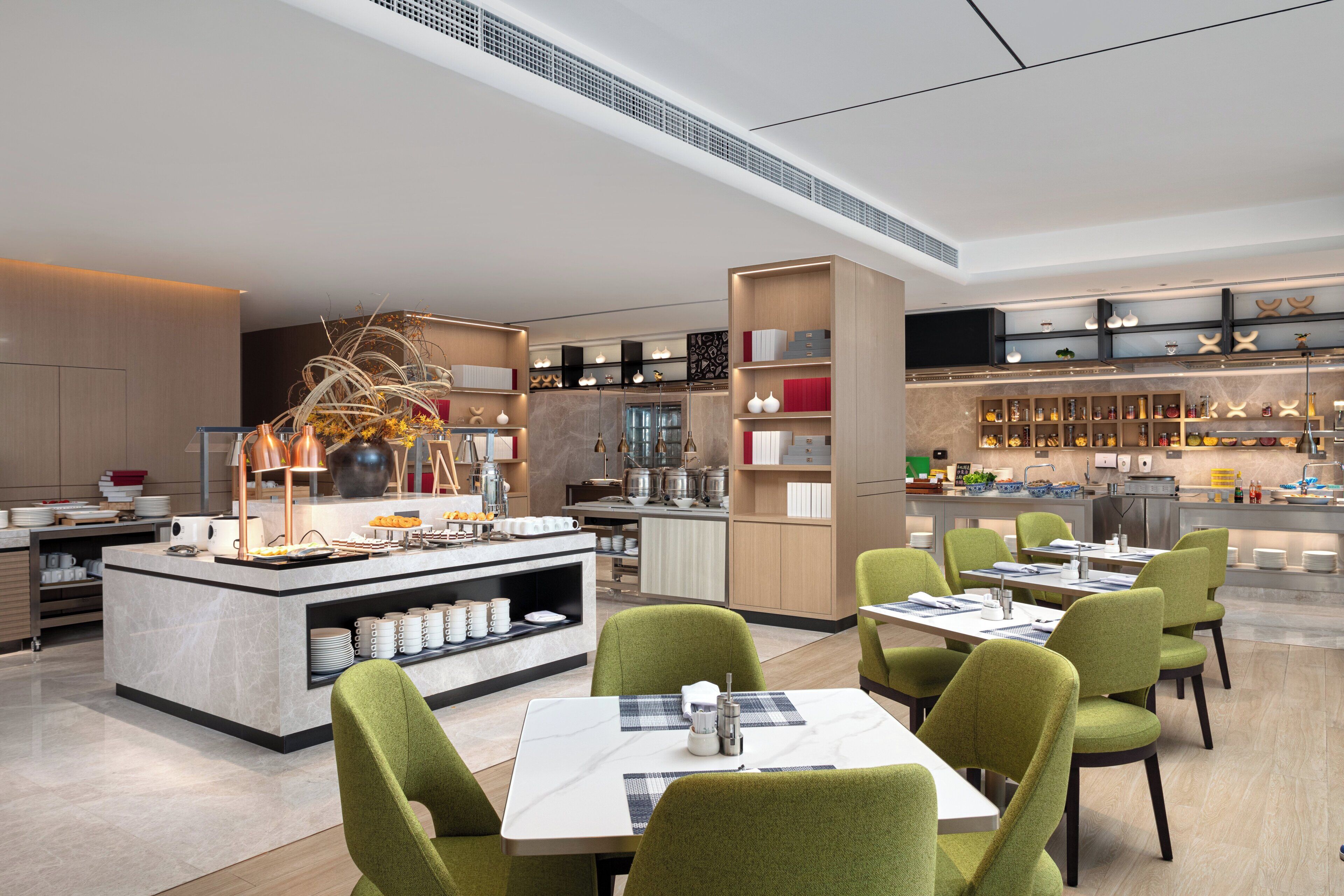 Un comedor moderno con una isla central, sillas tapizadas en verde y una variedad de electrodomésticos y unidades de almacenamiento al fondo.
