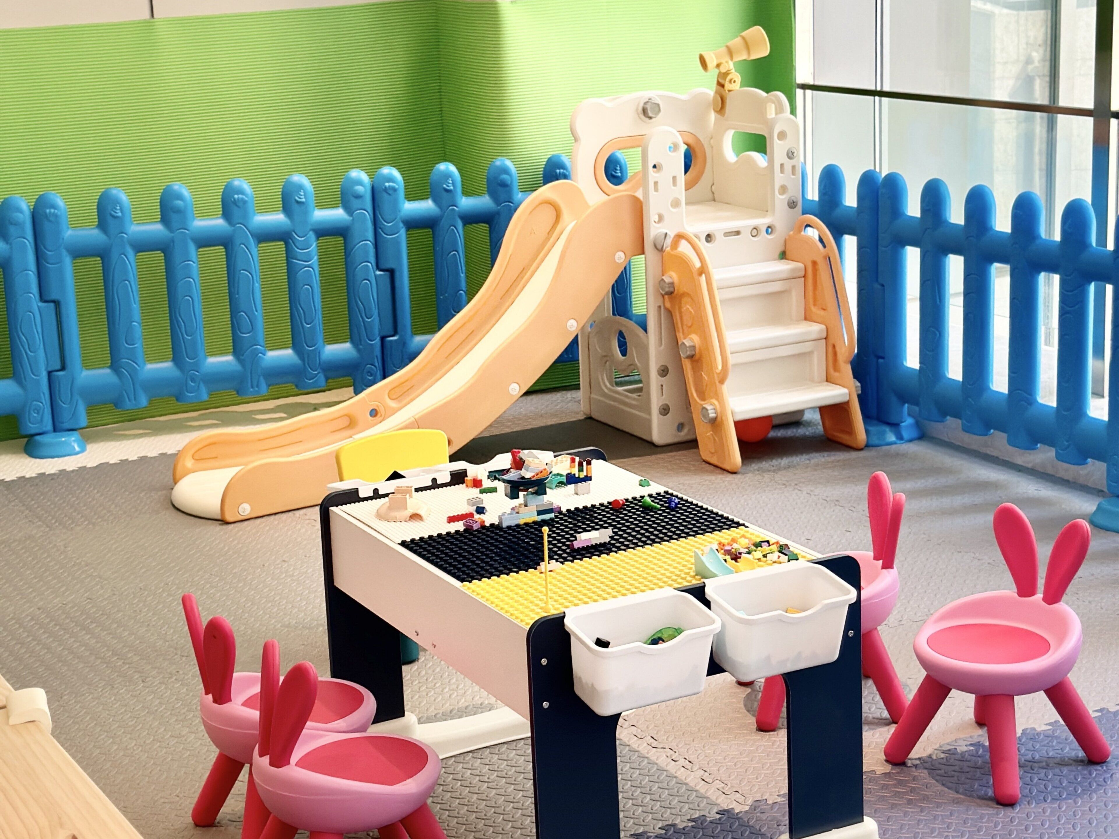 A children's play area with a slide, play structures, and a table with building blocks.