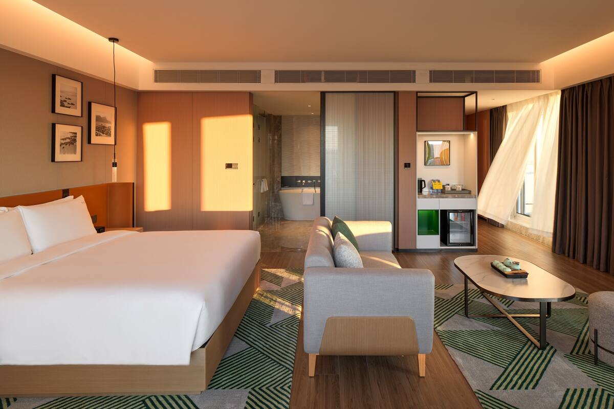 Una habitación de hotel con una cama grande, un sofá, una mesita y un kitchenette.