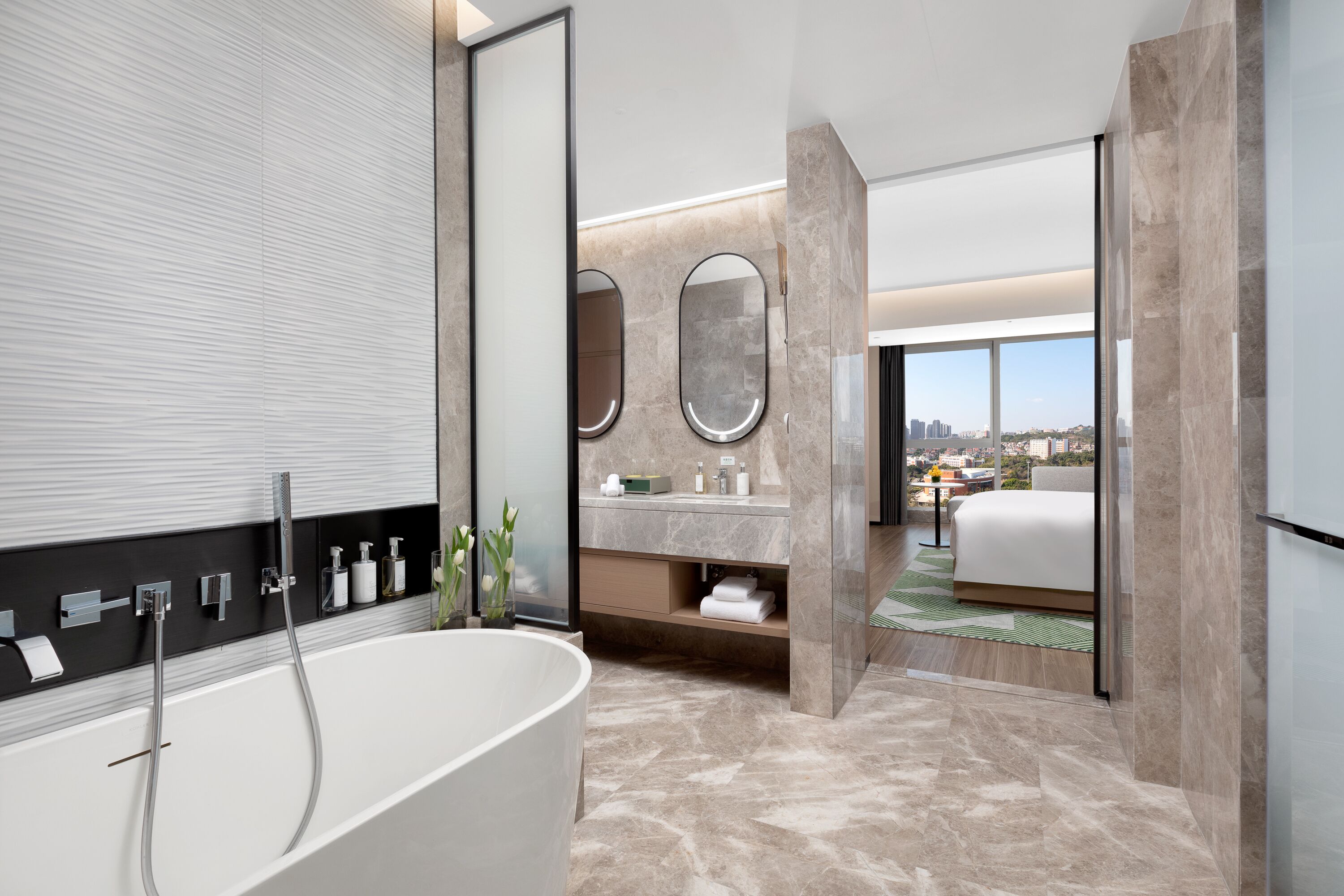 A modern bathroom with a freestanding bathtub, a vanity with a mirror, and a view of the city through large windows.