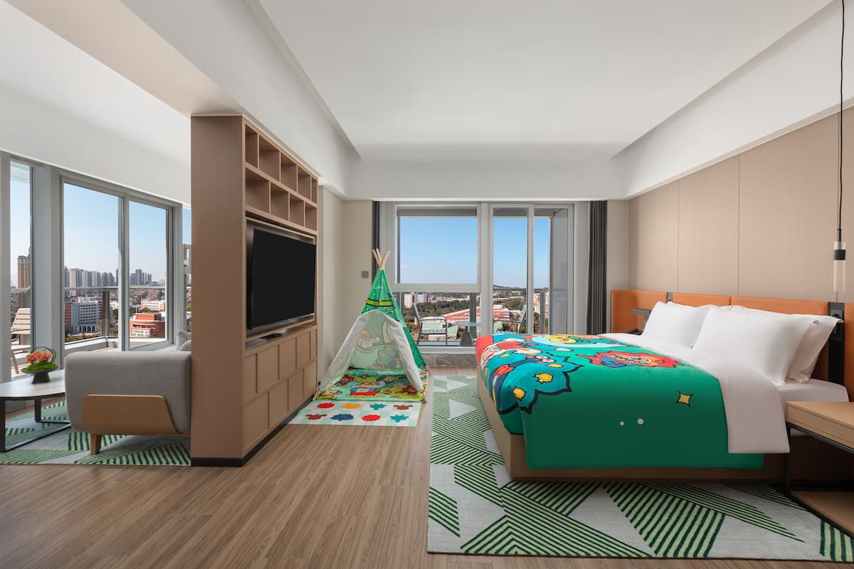 Una habitación de hotel moderna con una cama grande, televisión, zona de estar y vistas a la ciudad.