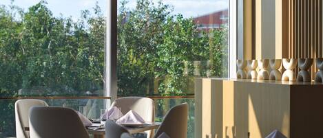 A dining area with a view of greenery and a building in the distance.