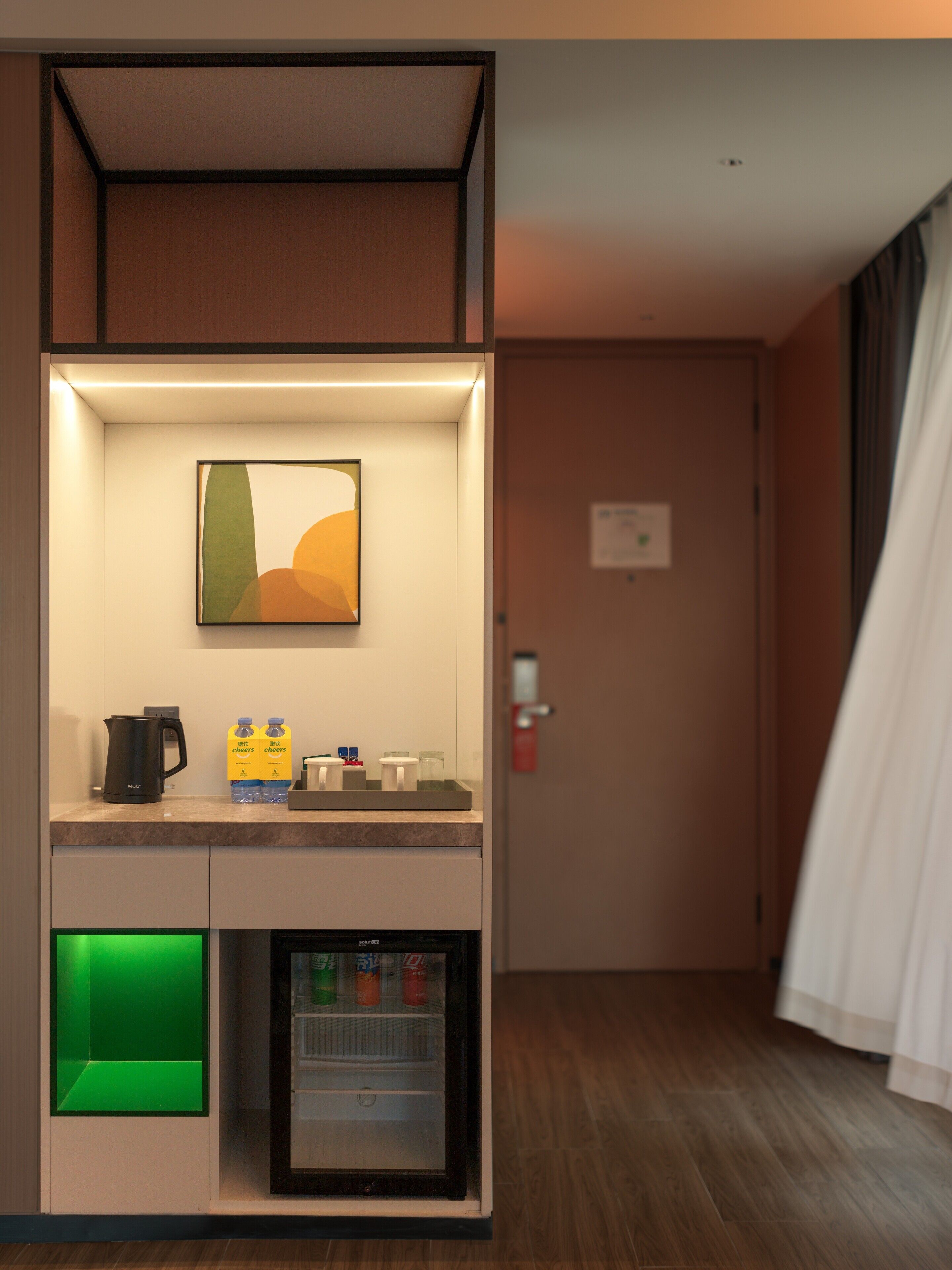 A modern hotel room with a kitchenette area, a mini-fridge, and a small refrigerator.