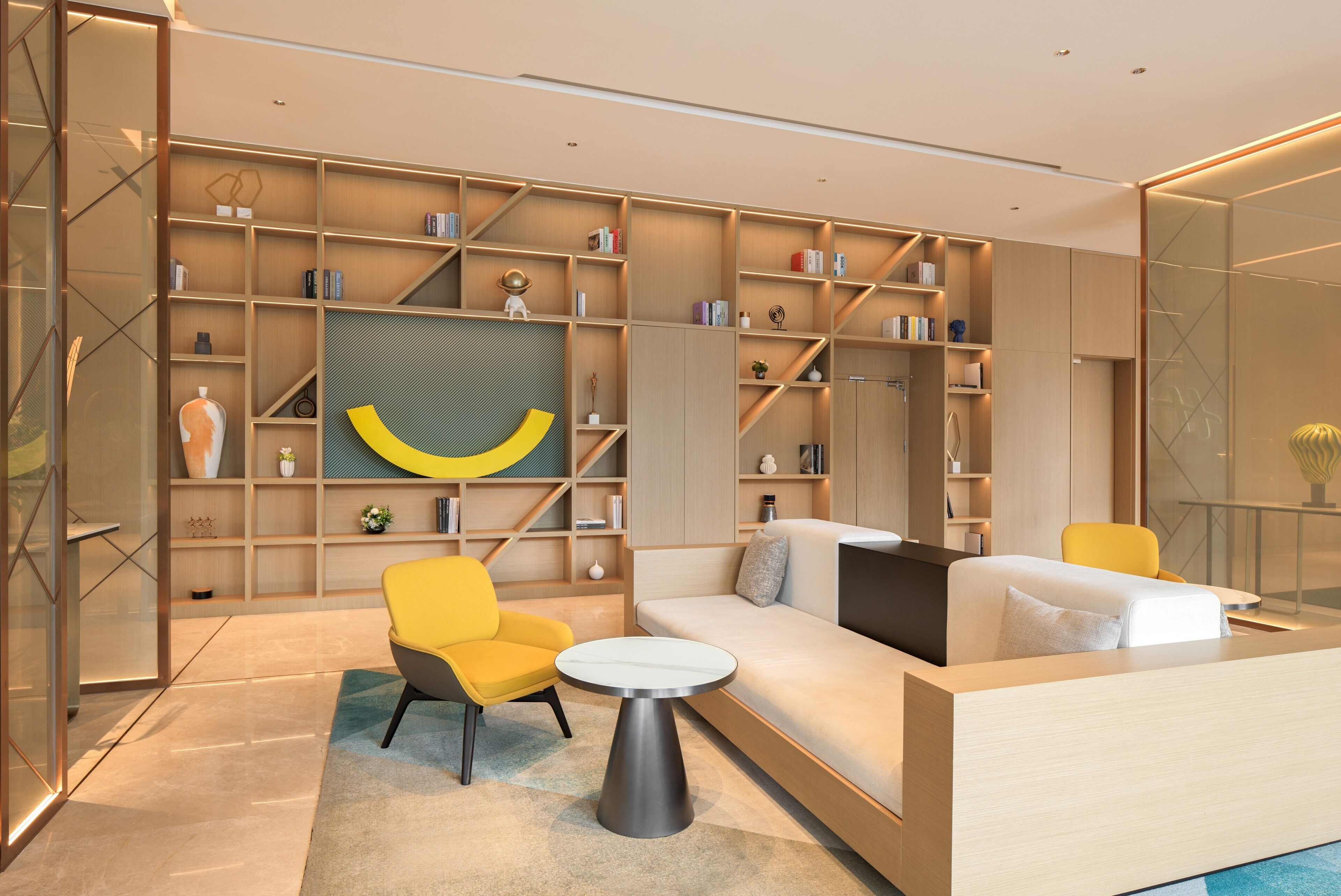 A modern living room with a sofa, a yellow armchair, a round coffee table, and a bookshelf filled with books and decorative items.