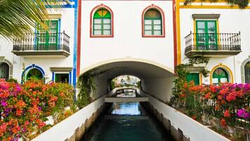 A canal with a bridge connecting two buildings, each with a balcony and a green door.