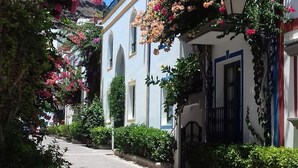 A narrow street with white buildings, arched doorways, and hanging flowers.
