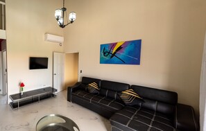 Un salon moderne avec un canapé en cuir noir, une table basse en verre et un tableau abstrait aux couleurs vives accroché au mur.