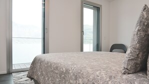 Un dormitorio con cama, una silla y vista a un cuerpo de agua a través de una puerta.