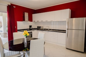 A modern kitchen with white cabinets, a stainless steel refrigerator, and a dining area with a glass table and white chairs.