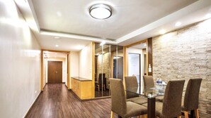 A modern hotel room with a wooden floor, a glass table with four chairs, a wooden cabinet, and a brick-patterned wall. - 3C - Short-Term Rental Allowed - Downtown Bkk Serviced Apartment (Krung Thep Maha Nakhon)