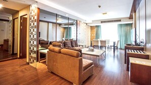 Ein modernes Hotelzimmer mit einer Couch, einem Esstisch, Stühlen, einer kleinen Küchenzeile und einem großen Fenster mit Vorhängen.