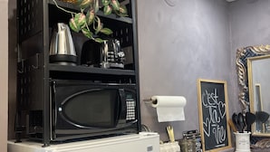A kitchen with a white refrigerator, black microwave, and stove. There is a basket with green leaves on top of the refrigerator. A chalkboard with writing is on the wall.