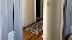 A hallway with wooden flooring, white walls, and a door leading to another room.