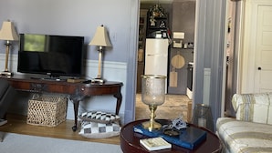A living room with a television, two lamps, a wooden coffee table with books, a patterned rug, and a checkered cushion.