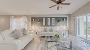 Un salon moderne avec un canapé blanc, une table basse en verre et un ventilateur de plafond.