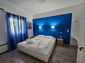 Hotellihuone, jossa on sänky, kaksi yöpöytää, yölamppu, taulu seinällä ja sininen verho.