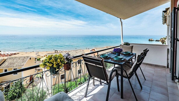 Un balcon avec une table et des chaises, donnant sur une plage et la mer.