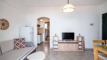 Ein modernes Wohnzimmer mit Sofa, Fernseher, Esstisch und einer Küche im Hintergrund.