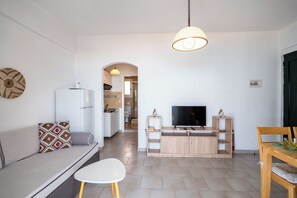 A modern living room with a sofa, a TV, a dining table, and a kitchen in the background.