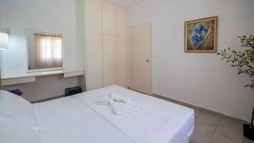 A hotel room with a bed, a wardrobe, a mirror, a painting, and a potted plant.