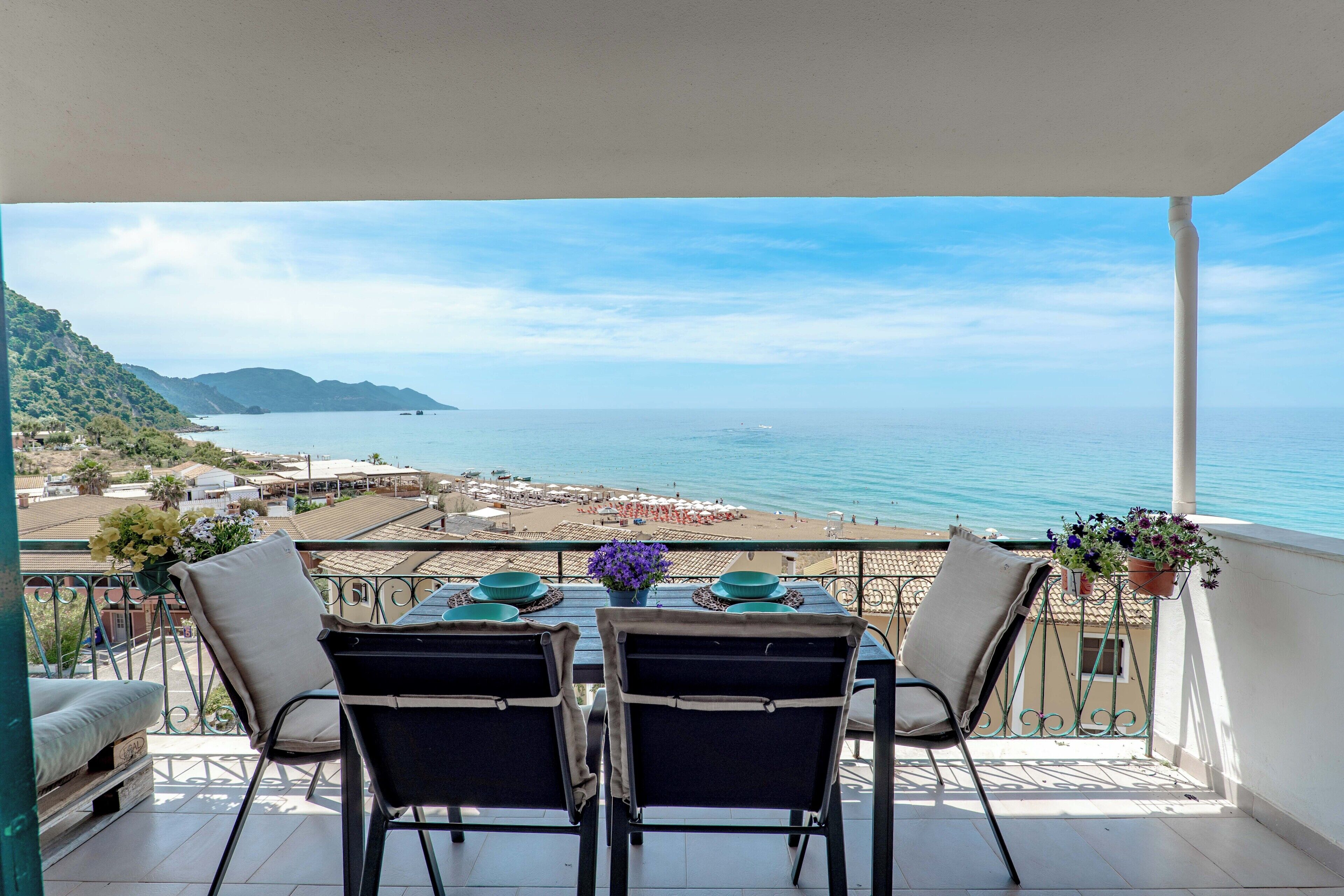 A balcony with a table set for two, overlooking a beach and the sea.
