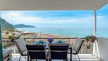 A balcony with a table set for two, overlooking a beach and the sea.