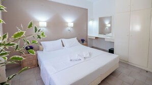 Un lit bien fait, avec du linge de lit blanc, une table de chevet avec une lampe, une armoire et un miroir fixé au mur.