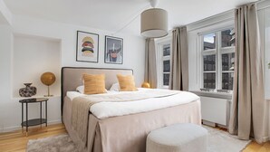 Et moderne soveværelse med en stor seng, et natbord, en lampe og et vindue med gardiner.