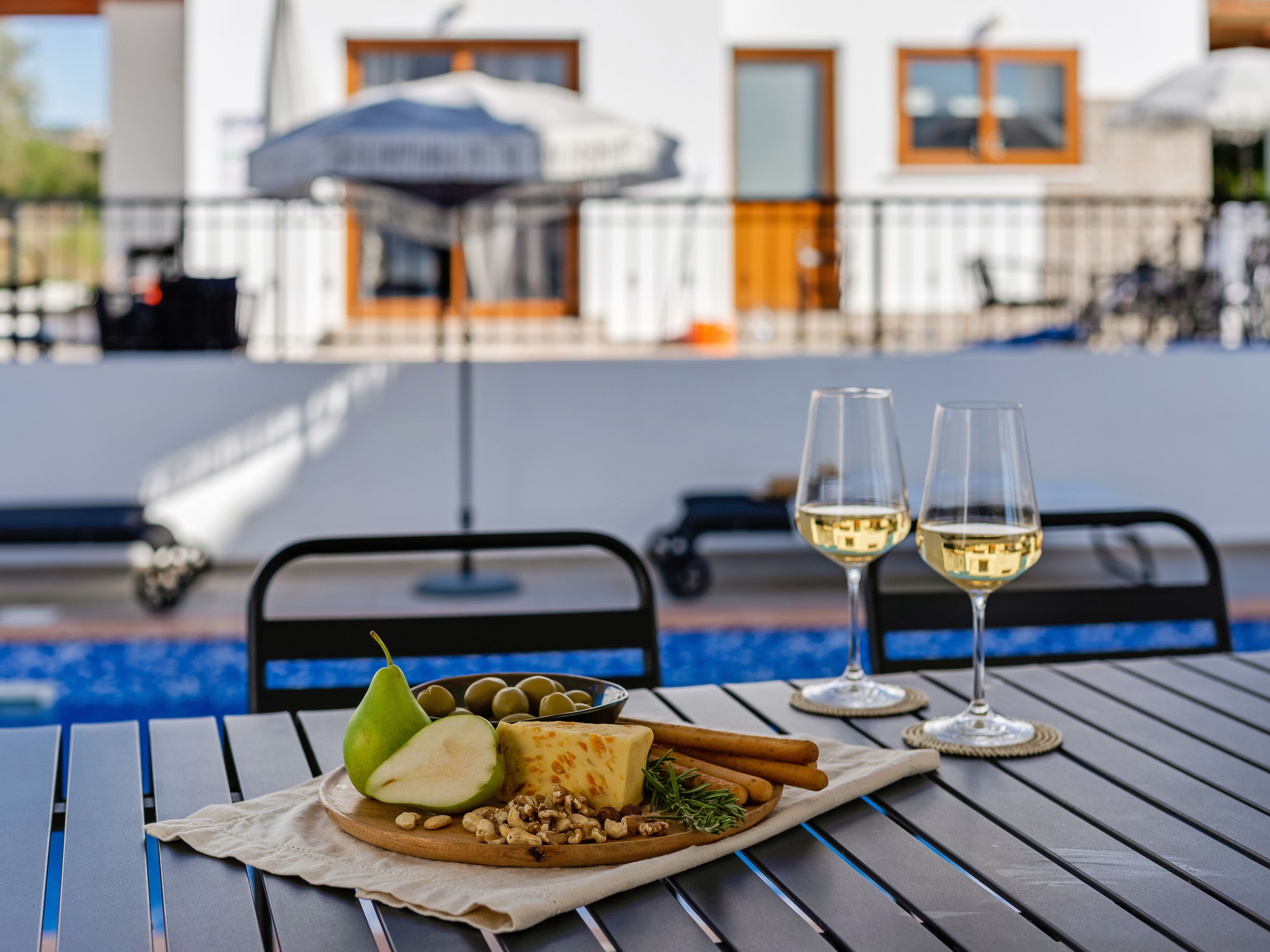 A dining table with a cheese platter, two glasses of white wine, and a pear.