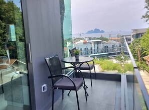 Un balcone con due sedie e un tavolino, affaccia su un panorama urbano con edifici e una montagna in lontananza.