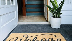 Un paillasson sur lequel est inscrit : « Bienvenue à vos amis et à votre famille », placé à l’entrée d’une maison.