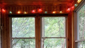 L’intérieur d’une cabane avec des murs en bois, deux grandes fenêtres, un fauteuil gris et une pile de caisses en bois.