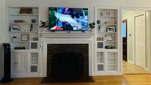 Un salon doté d’une cheminée, d’un téléviseur fixé au mur et d’étagères intégrées où sont exposés des objets décoratifs.