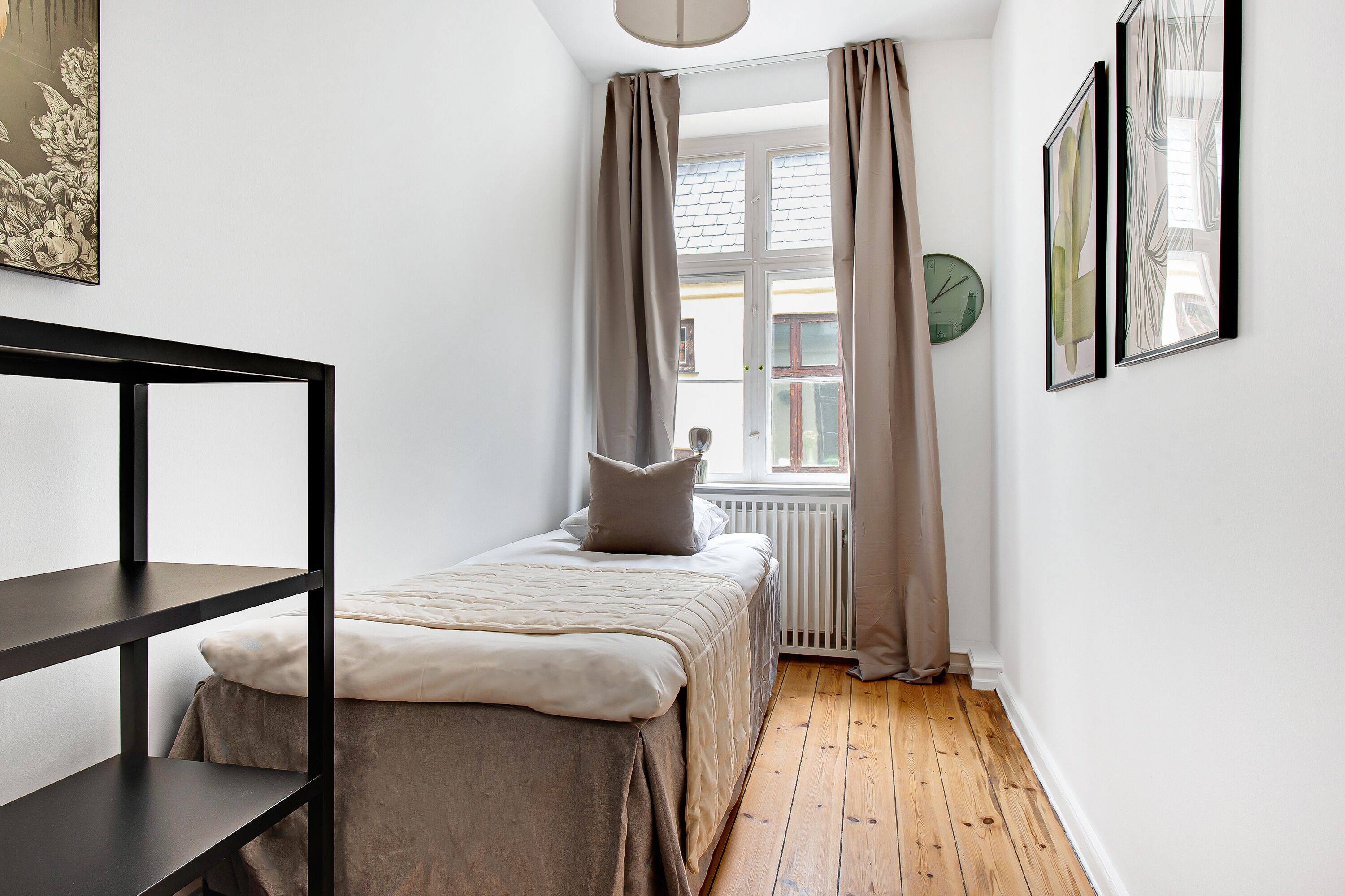 Un dormitorio pequeño y bien iluminado con una cama individual, un radiador y una ventana con cortinas.
