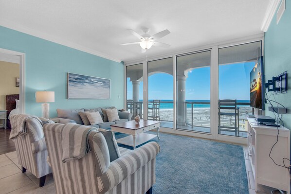 Una sala de estar con vista a la playa, un ventilador de techo y un televisor sobre un mueble.