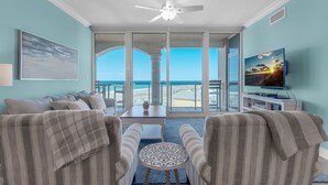 Una sala de estar con vista a la playa, ventilador de techo, televisor y mesa de centro con estampado.