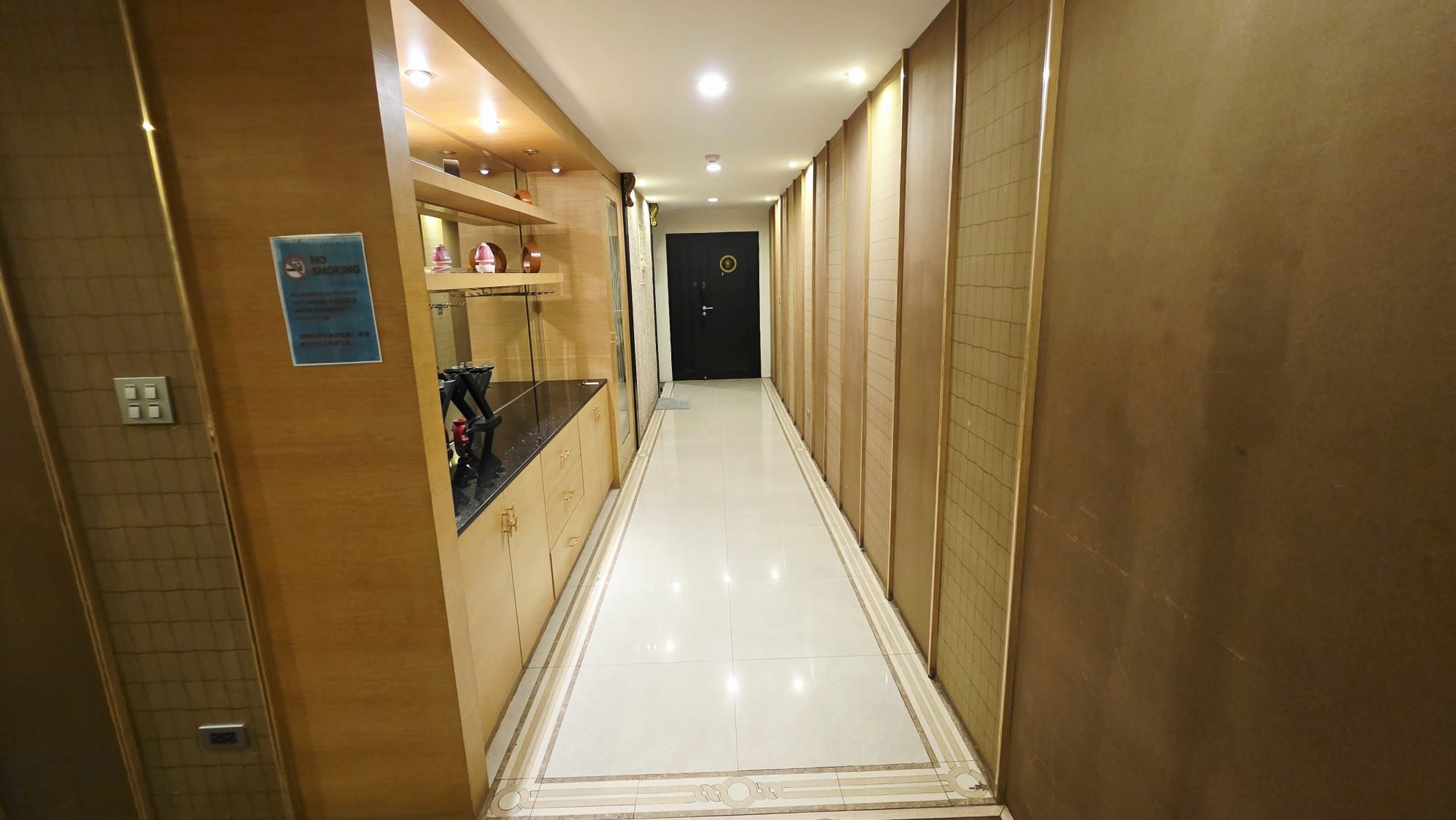 A hotel hallway with a reflective floor, a no-smoking sign, and a door at the end.
