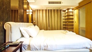 Een hotelkamer met een groot bed, een nachtkastje met een afstandsbediening, een spiegel en een kledingkast met planken.