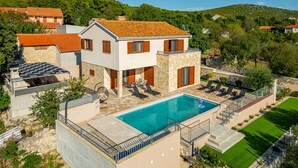 A two-story villa with a swimming pool, stone walls, and a view of the surrounding hills.