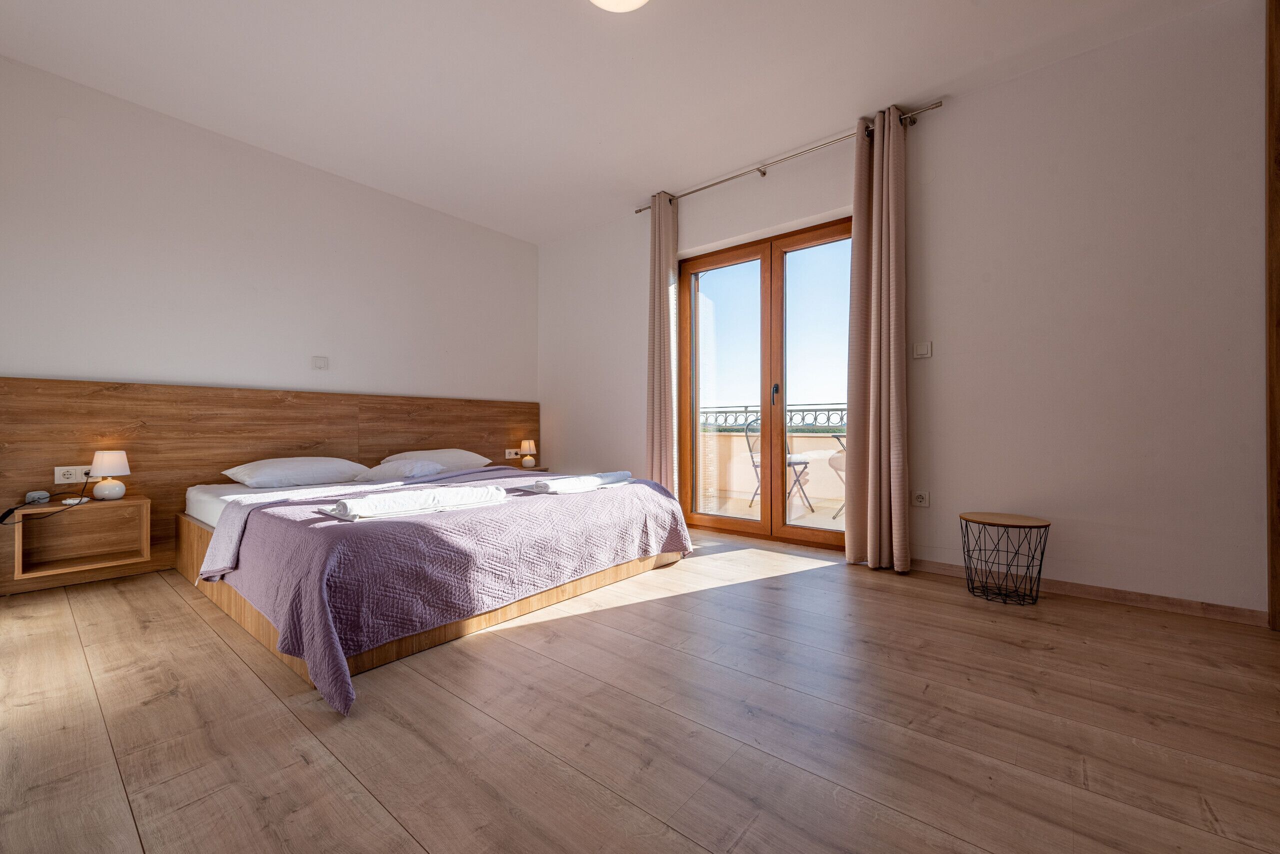 Une chambre avec un plancher en bois, un lit doté d’une tête de lit, une table de chevet, une petite table et une vue sur l’extérieur grâce à une porte coulissante.