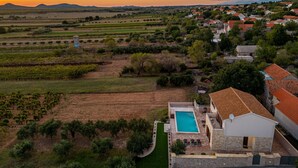 A villa with a swimming pool, surrounded by vineyards and a village.