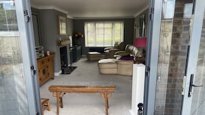 Een open schuifdeur naar een woonkamer met een open haard, leren banken, een houten bankje en een eettafel.