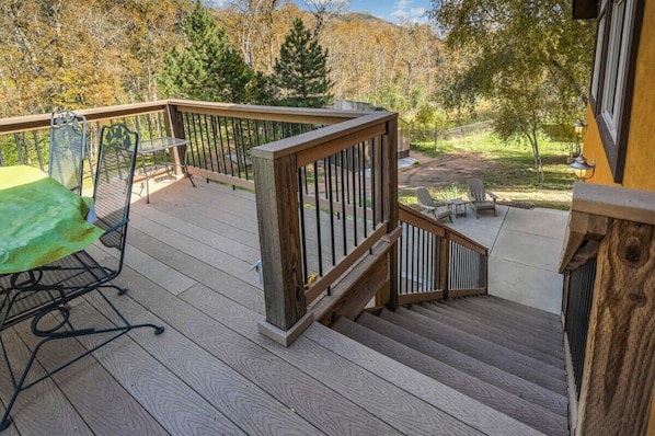 A wooden deck with a metal railing, a table with chairs, and a view of a forested area.