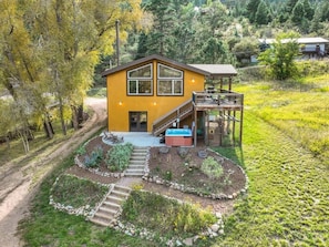 A yellow house with a deck, a hot tub, and a staircase leading to the entrance.